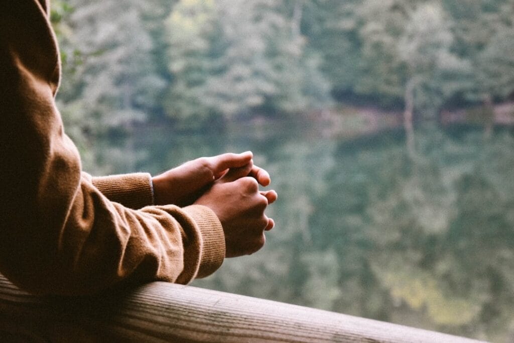 Image of a person leaning on a railing overlooking a pond. 