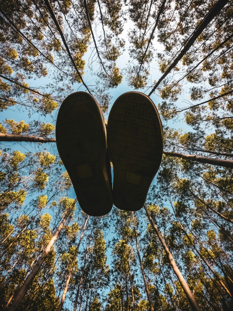 View from underneath shoes. Looking at the soles of shoes up to the sky with trees around. 