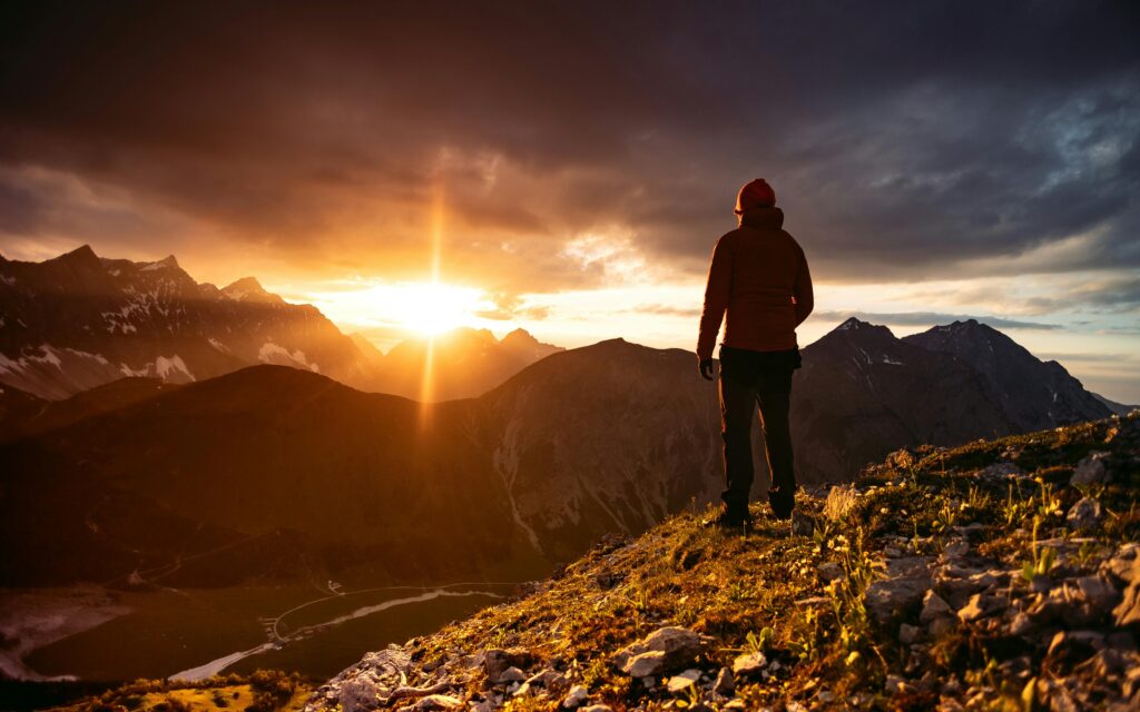 Person overlooking a mountain scape with the sun beaming over the ridge. 